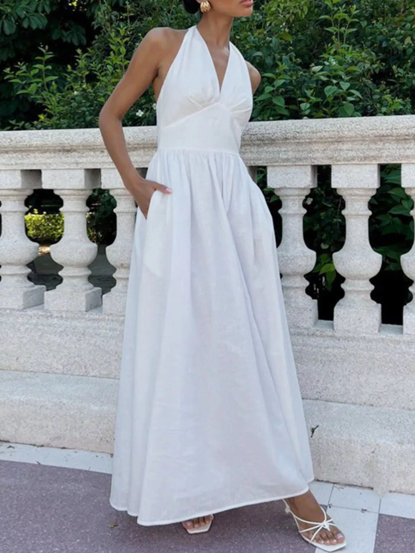 Woman in a white halter neck dress standing against a decorative stone wall.
