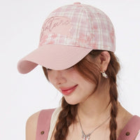 Person wearing a pink plaid baseball cap with 'Adventure' text on a white background