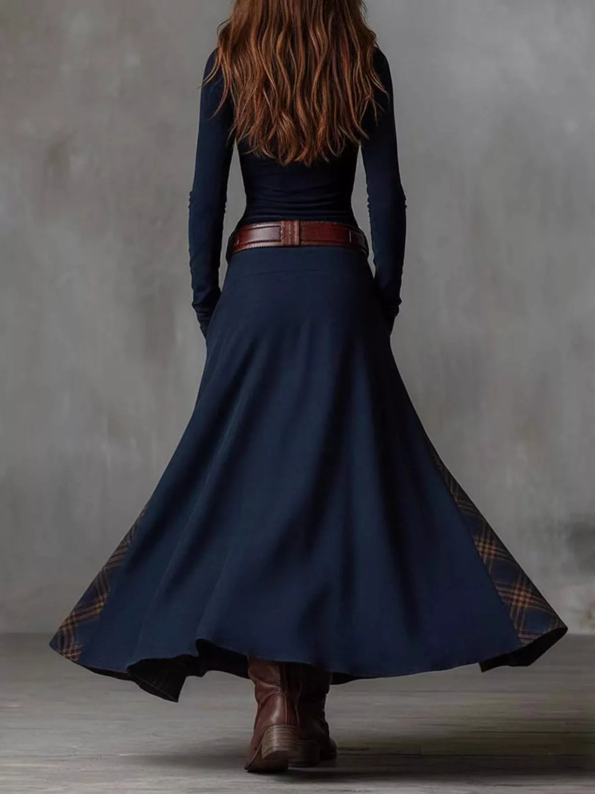 Person wearing a long navy blue dress with a belt and brown boots against a gray background