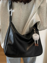 Black handbag with a fluffy keychain held by a person wearing a light gray hoodie.
