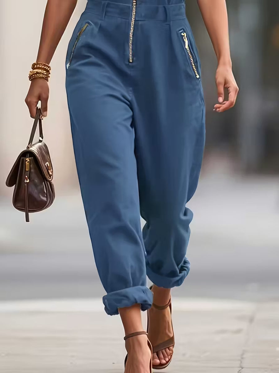 Person wearing blue pants with zippers, holding a brown handbag on a blurred background