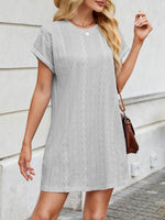 Woman wearing a gray lace dress against a light-colored wall.