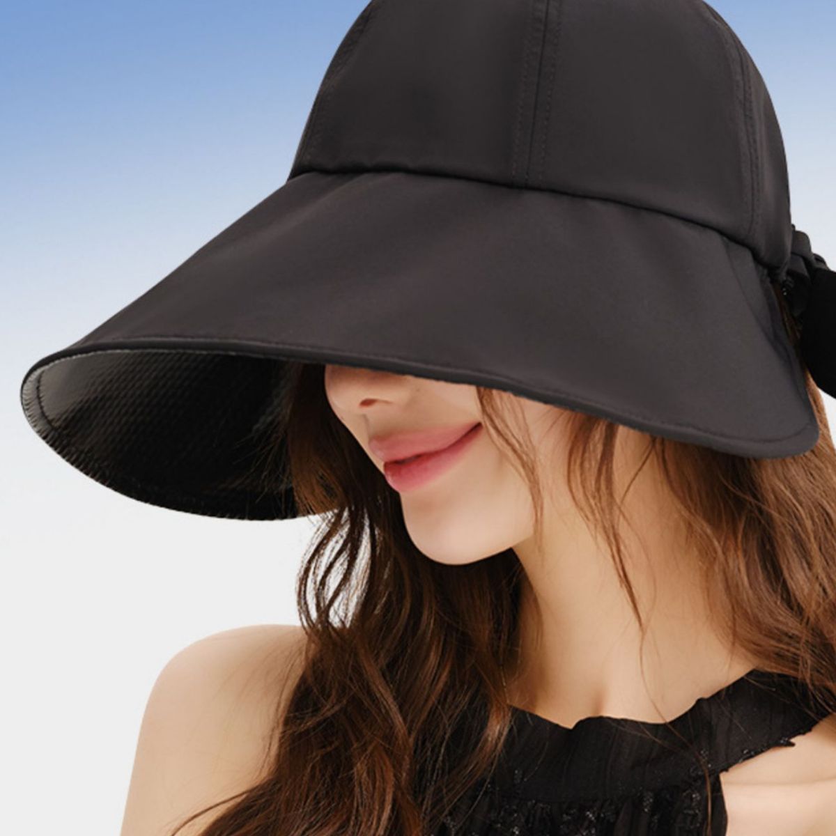 Woman wearing a black sun hat against a clear blue sky