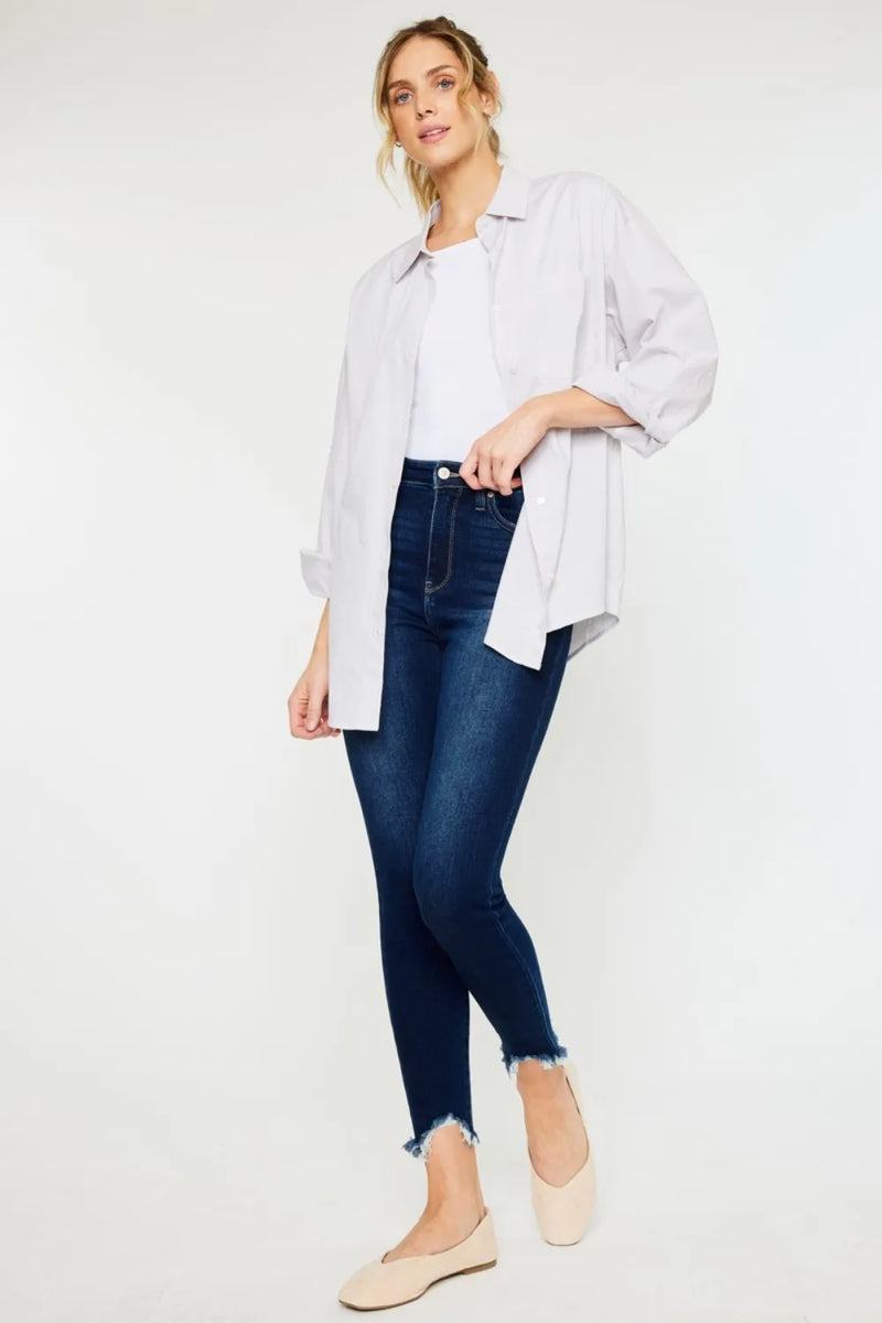 Woman wearing a light gray shirt, white top, dark blue jeans, and beige flats on a white background