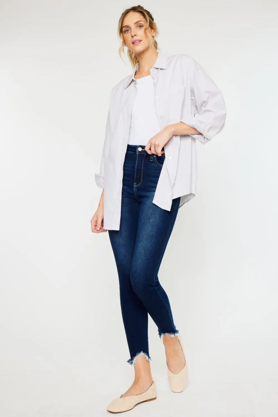 Woman wearing a light gray shirt, white top, dark blue jeans, and beige flats on a white background