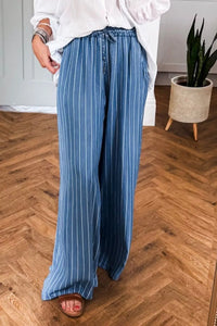 Person wearing blue striped pants on a wooden floor with a plant in the background