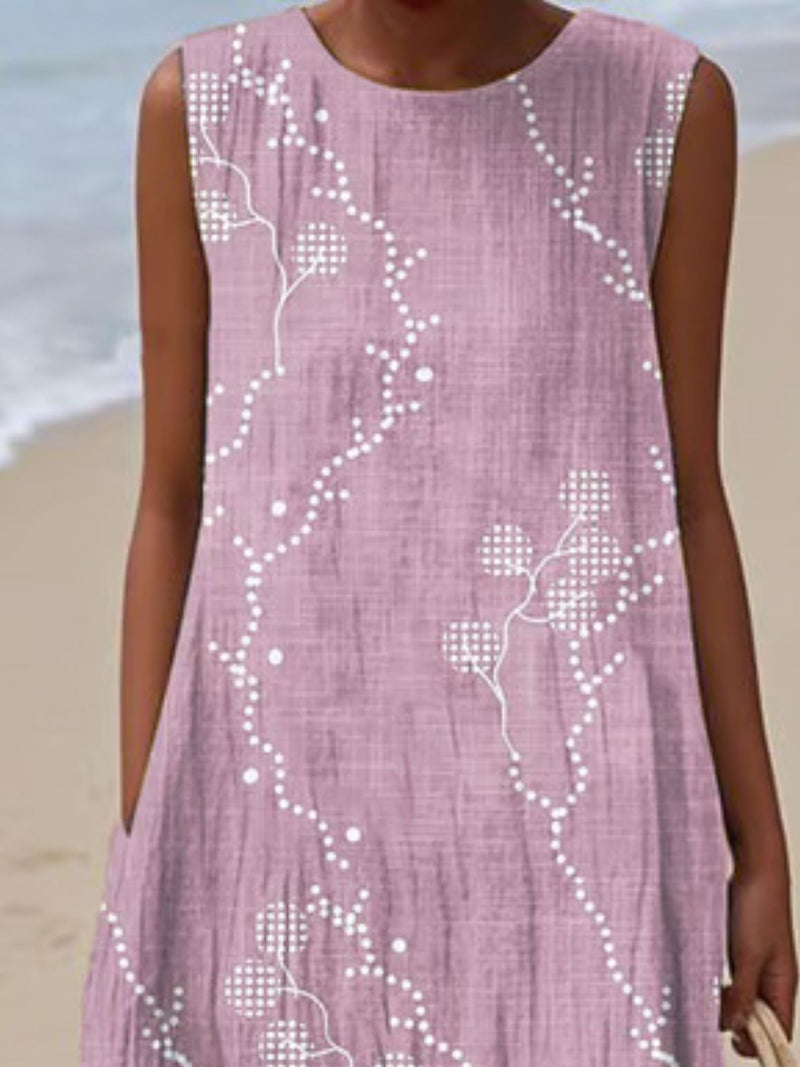 Person wearing a pink dress with white floral patterns on a beach.