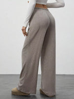 Person wearing beige ribbed wide-leg pants and a white long-sleeve top against a plain background