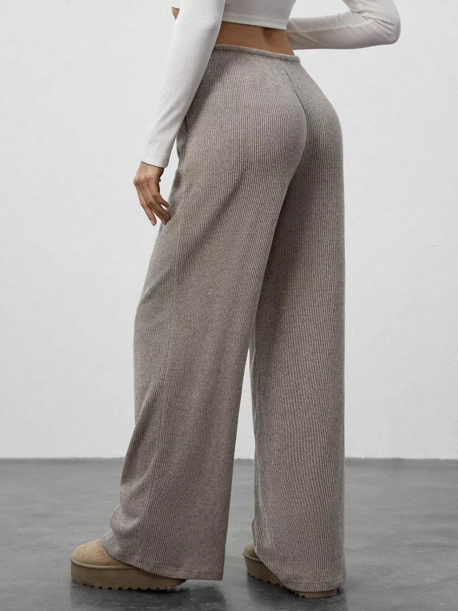 Person wearing beige ribbed wide-leg pants and a white long-sleeve top against a plain background
