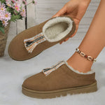 Brown slippers with tassel details held by a hand on a light background