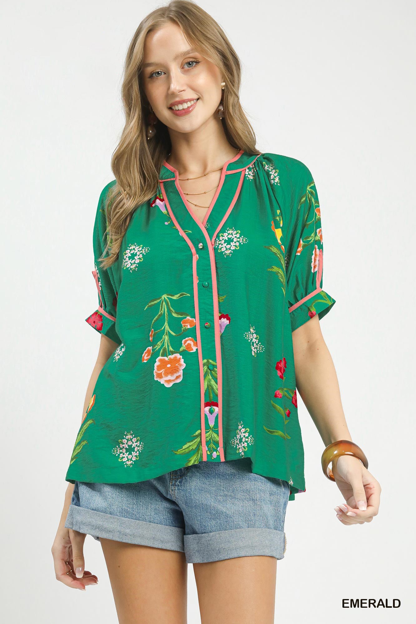 Woman wearing a green floral blouse with denim shorts on a white background