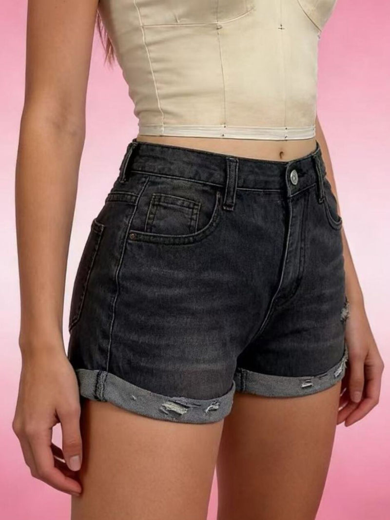 Person wearing black denim shorts on a pink background