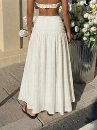 Person wearing a white pleated skirt and top in an outdoor setting with flowers.