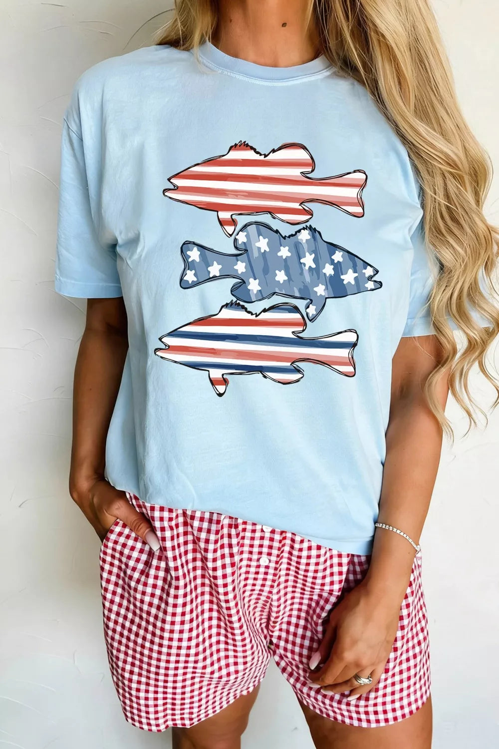 Light blue t-shirt with fish graphic and red checkered shorts on a plain background