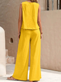 Woman wearing a yellow sleeveless top and wide-leg pants against a beige wall.