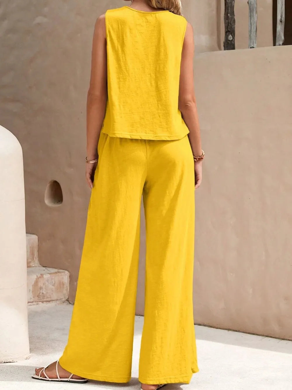 Woman wearing a yellow sleeveless top and wide-leg pants against a beige wall.