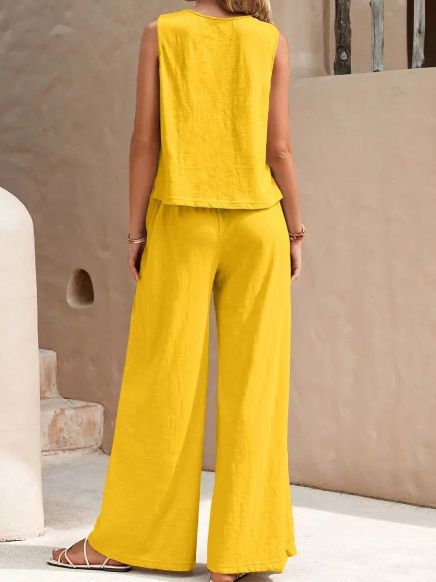 Woman wearing a yellow sleeveless top and wide-leg pants against a beige wall.