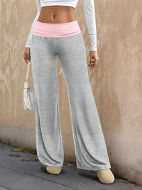 Person wearing gray wide-leg pants with a pink waistband against a beige wall.