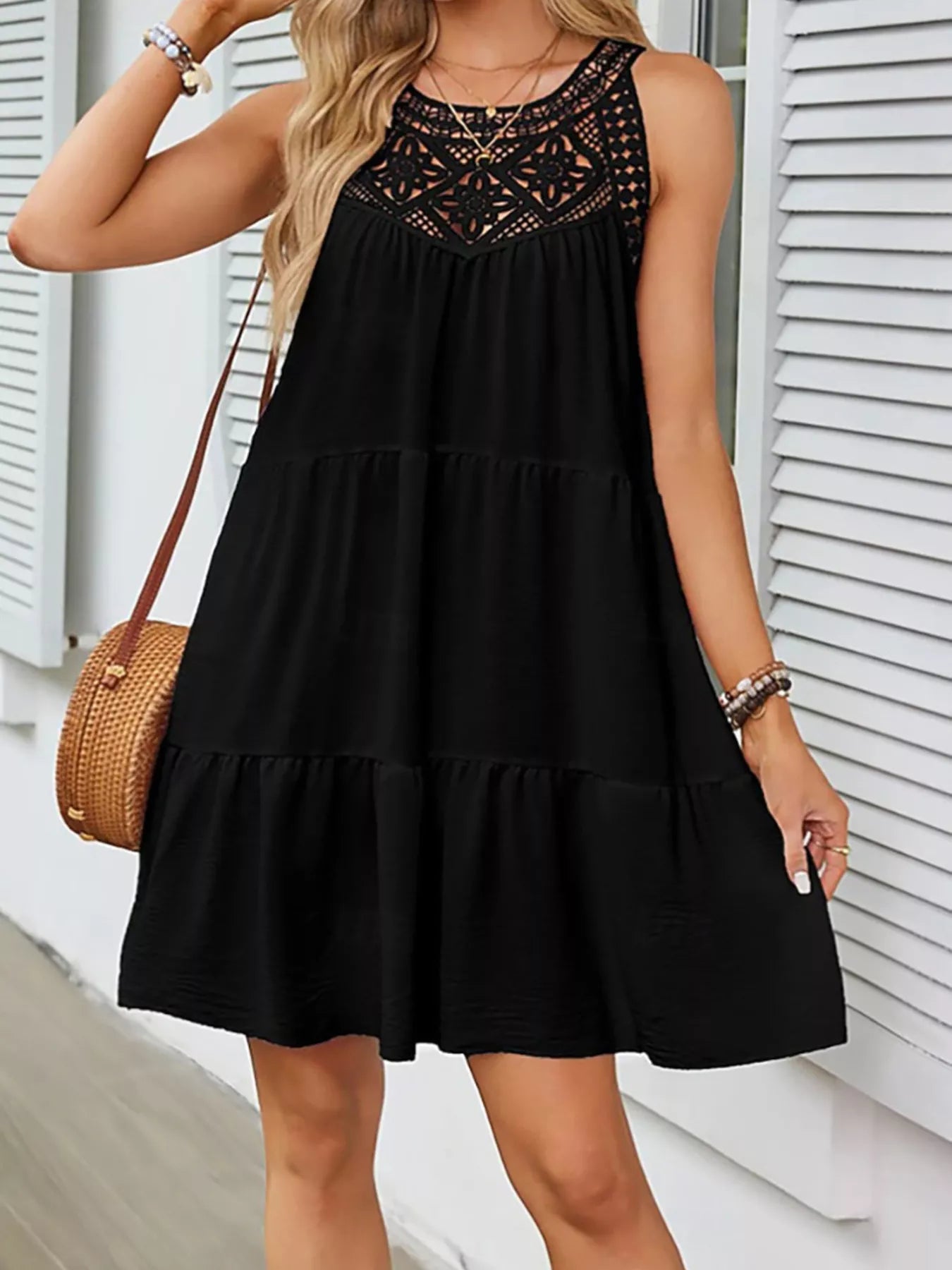 Woman wearing a black dress with lace details, standing against a white wall.