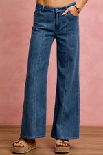 Person wearing blue wide-leg jeans against a pink background