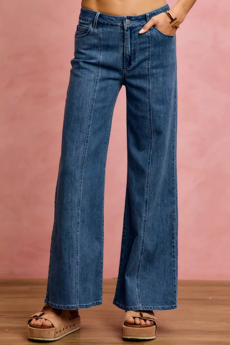 Person wearing blue wide-leg jeans against a pink background