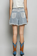 Person wearing denim shorts with rhinestone accents and cowboy boots on a plain background