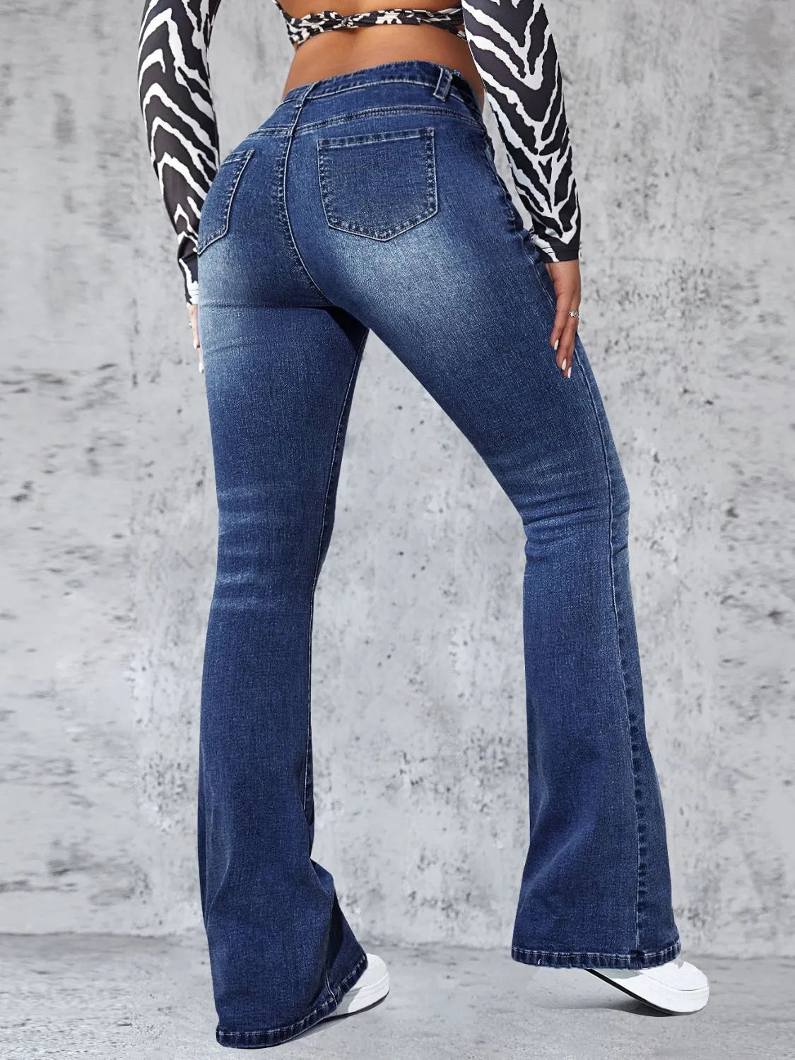 Person wearing blue flared jeans with a zebra print top against a gray concrete wall.
