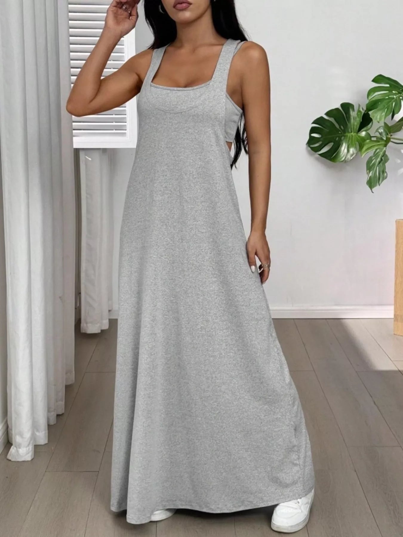 Woman wearing a gray maxi dress in a room with white walls and a plant.