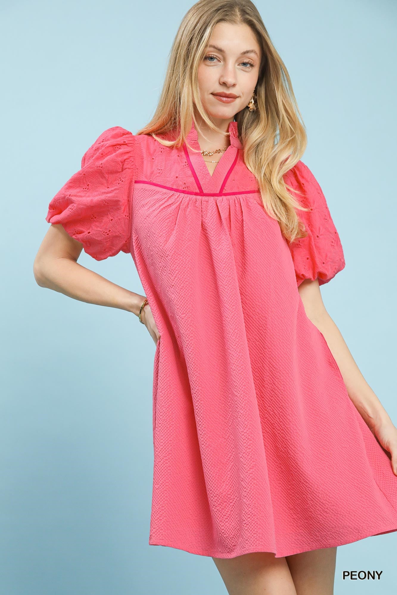 Woman wearing a pink dress with puff sleeves against a light blue background