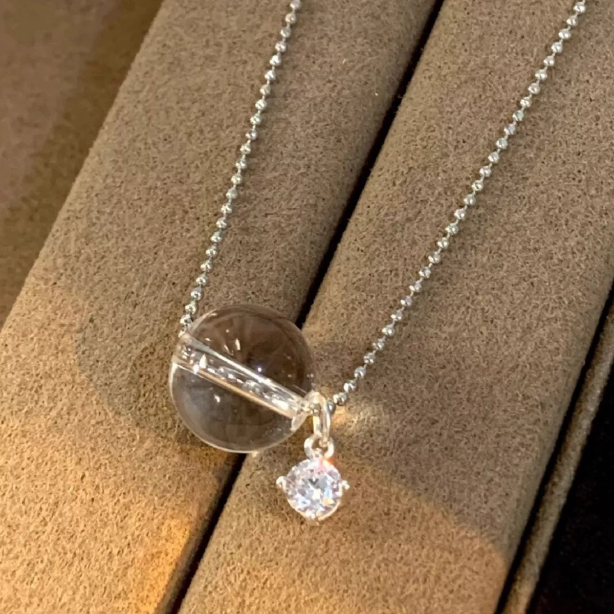 Necklace with a clear pendant and small round charm on a wooden surface