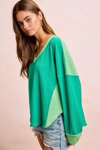 Woman wearing a green color-blocked sweater against a pink background