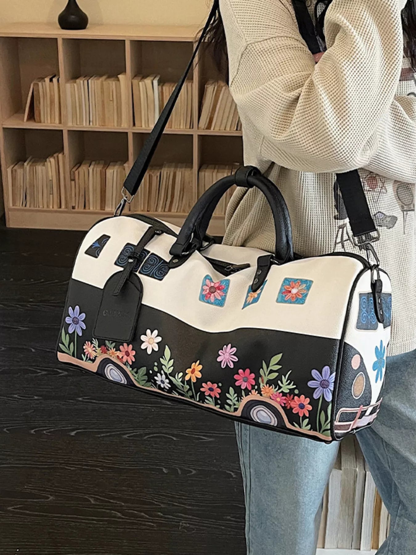 Person holding a floral-patterned duffel bag in front of a bookshelf.