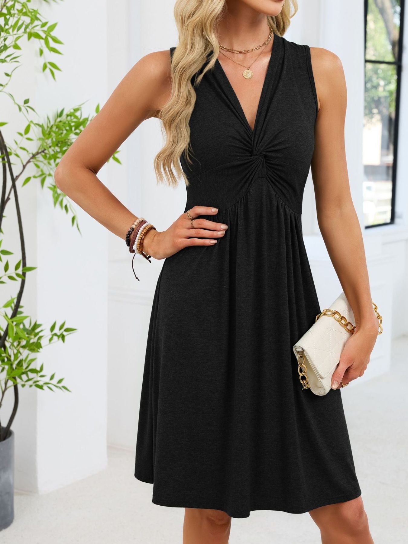 Woman wearing a black dress holding a white clutch in a bright room.