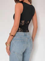 Person wearing a black sleeveless top with lace details and light blue jeans on a plain background