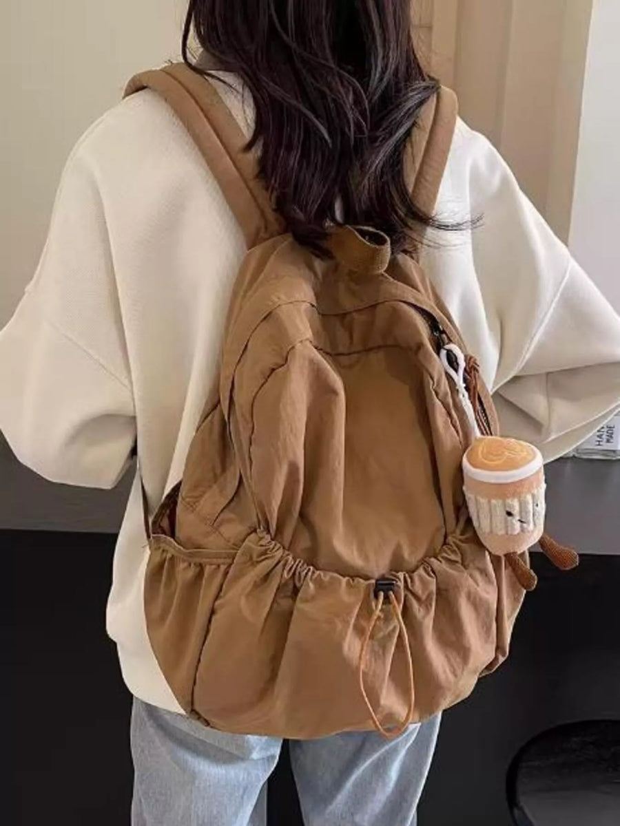 Person wearing a brown backpack holding a small plush toy.