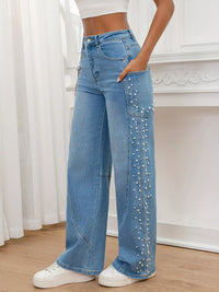 Person wearing blue jeans with pearl embellishments in a minimalistic setting.