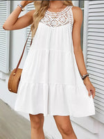 Woman wearing a white dress with lace details in front of a white wall.