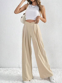 Woman wearing a white top and beige wide-leg pants against a white background