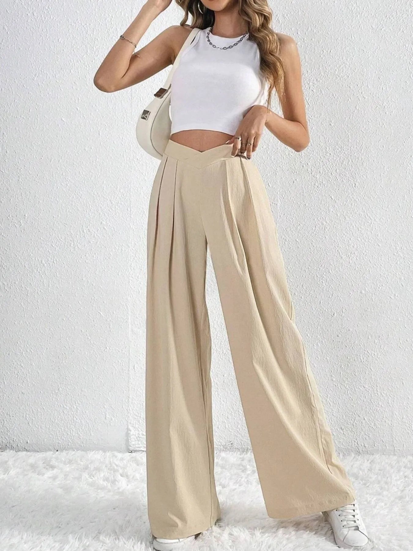 Woman wearing a white top and beige wide-leg pants against a white background