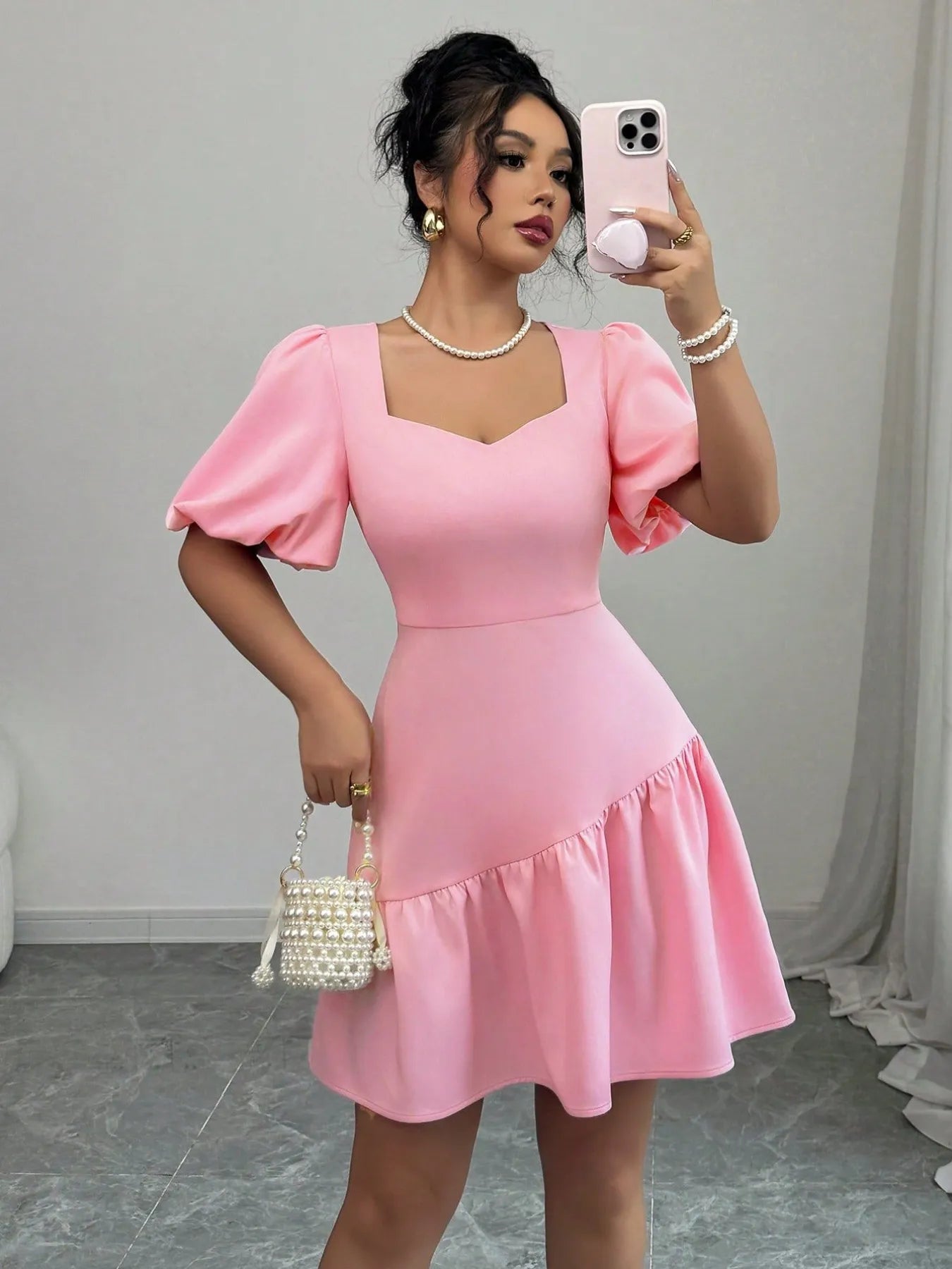 Woman taking a mirror selfie wearing a pink dress with puffed sleeves.