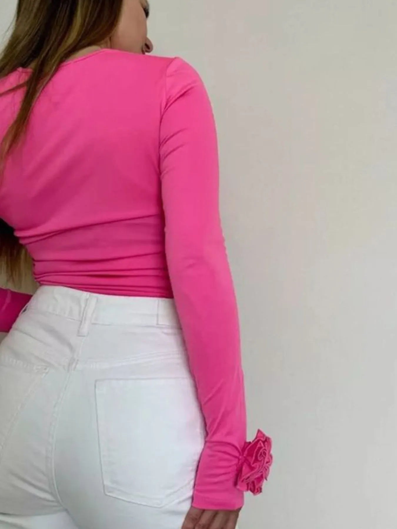Person wearing a bright pink long-sleeve top with a flower detail on a plain background