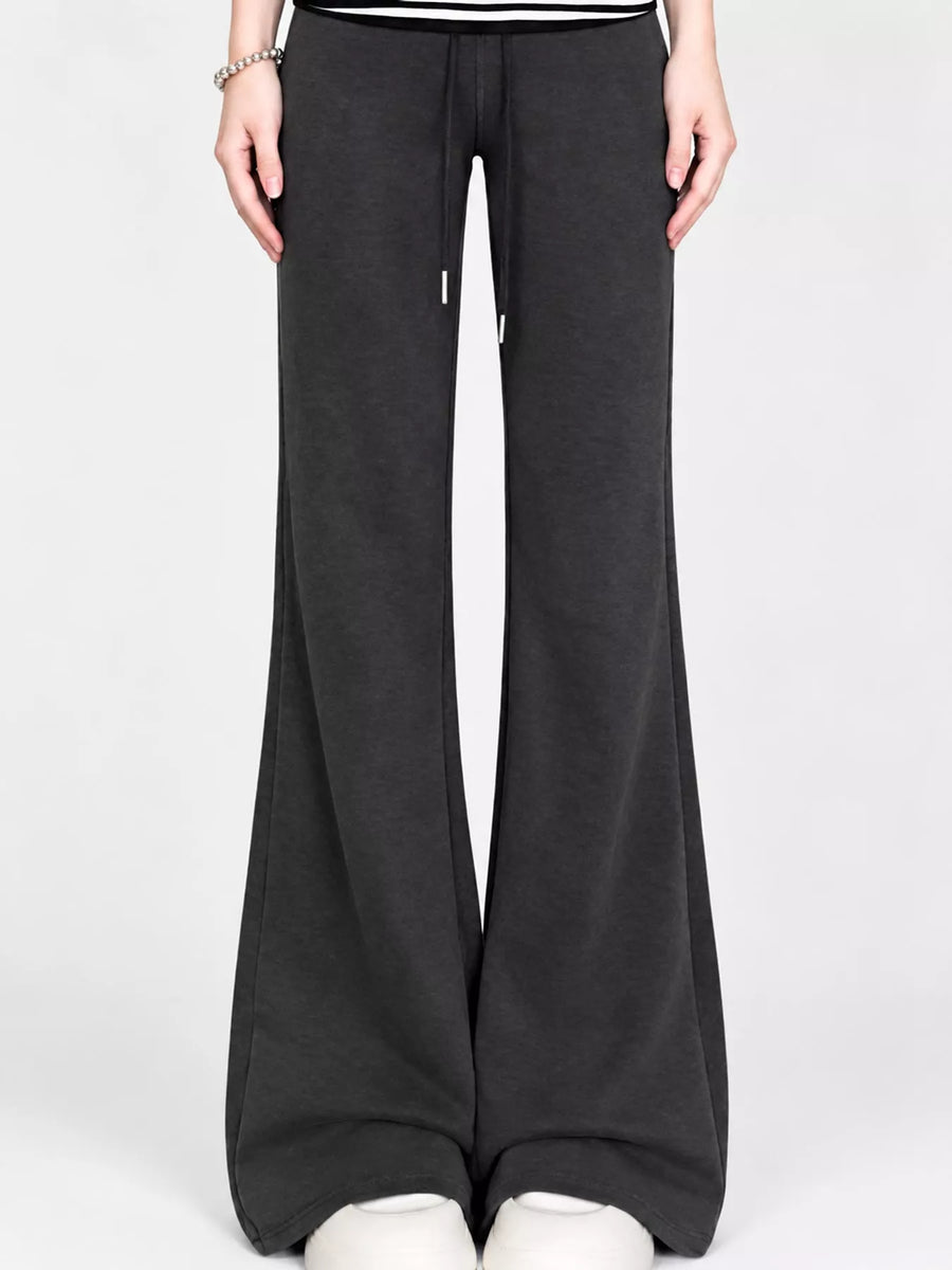 A person wearing dark charcoal wide-leg sweatpants with a drawstring waist, paired with a black and white top and white sneakers, shown against a light gray studio background.