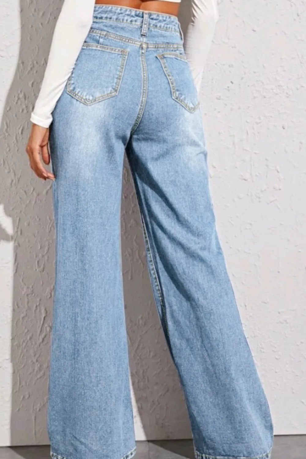 Light blue wide-leg jeans worn by a person against a gray wall.
