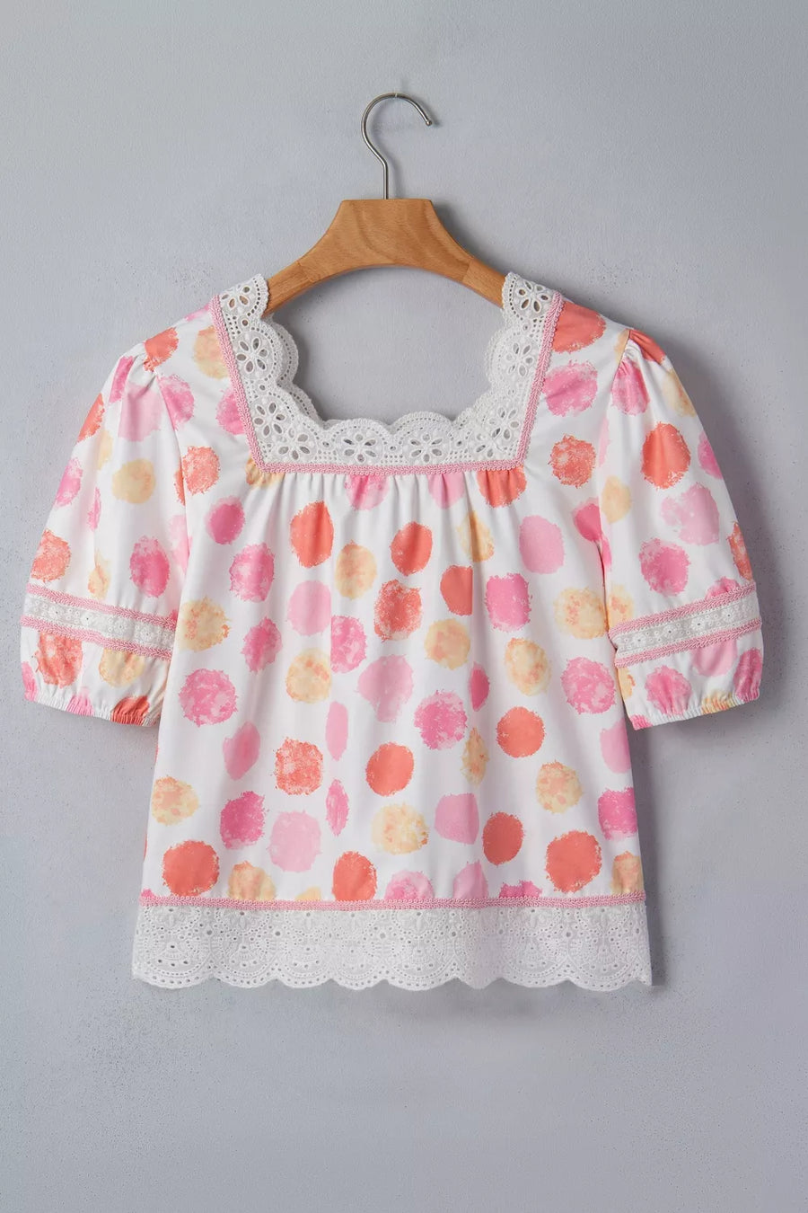 Floral blouse with lace details on a wooden hanger against a gray background