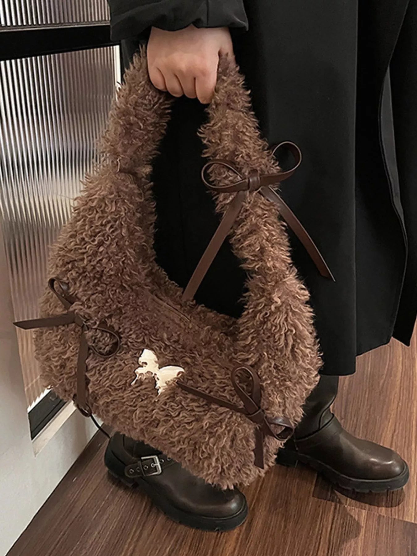 Brown fluffy bag held by a person wearing black shoes on a wooden floor.