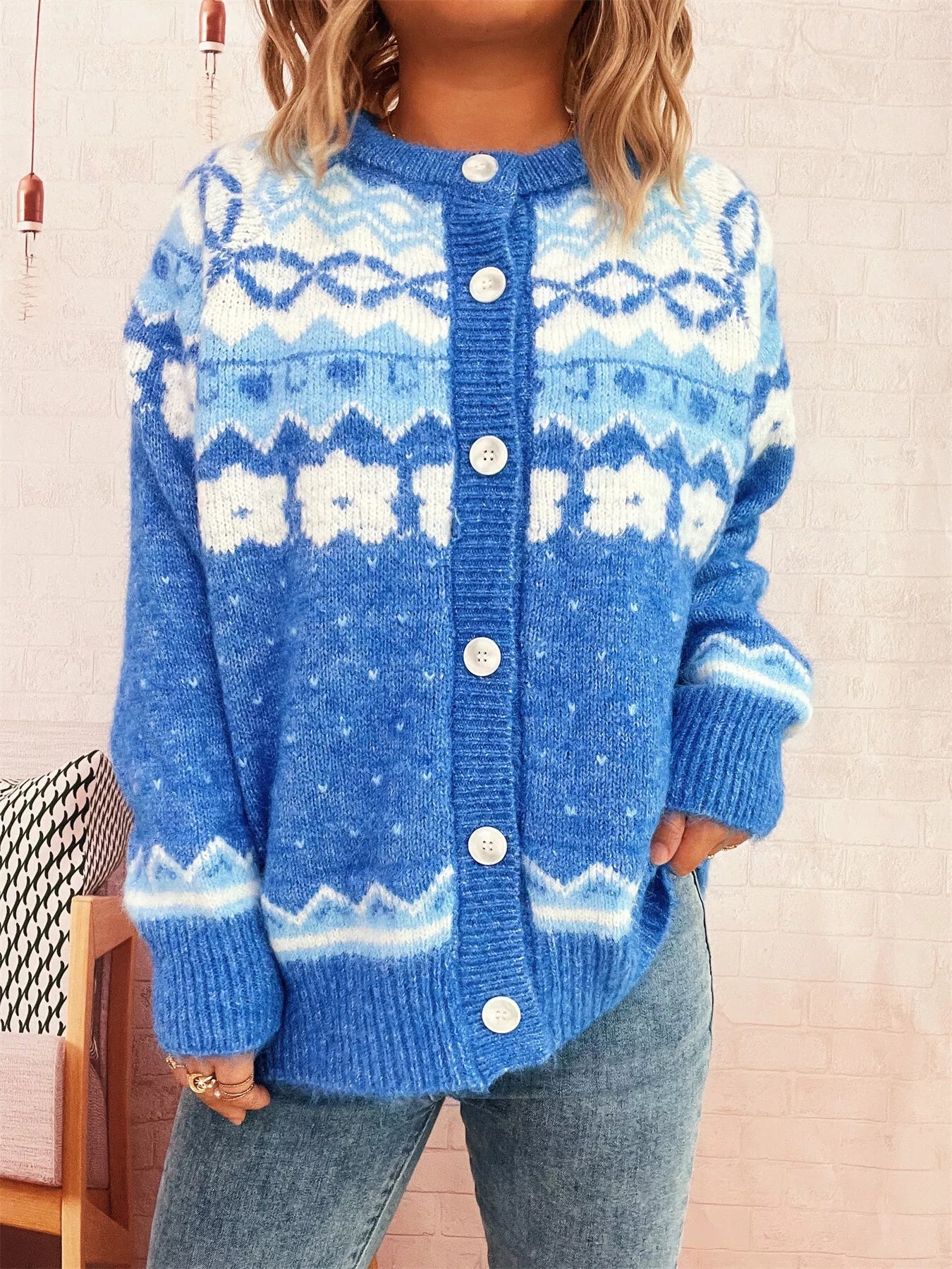 Person wearing a blue knitted cardigan with white patterns on a neutral background