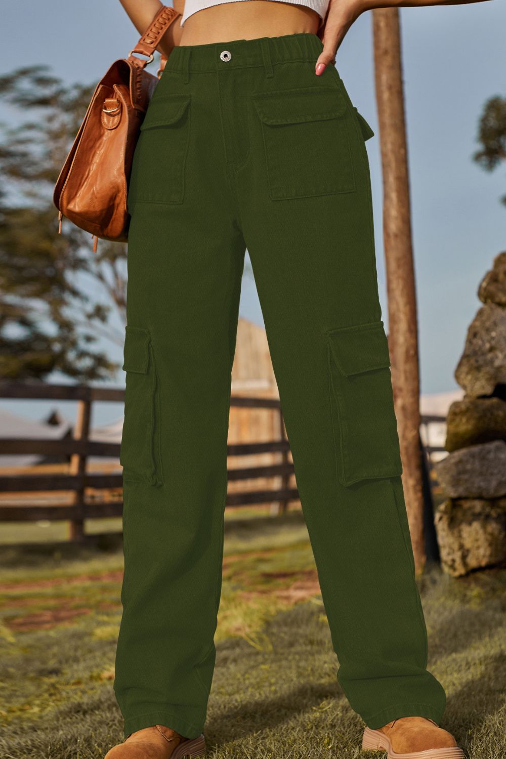 Person wearing green pants with a brown leather bag in an outdoor setting.
