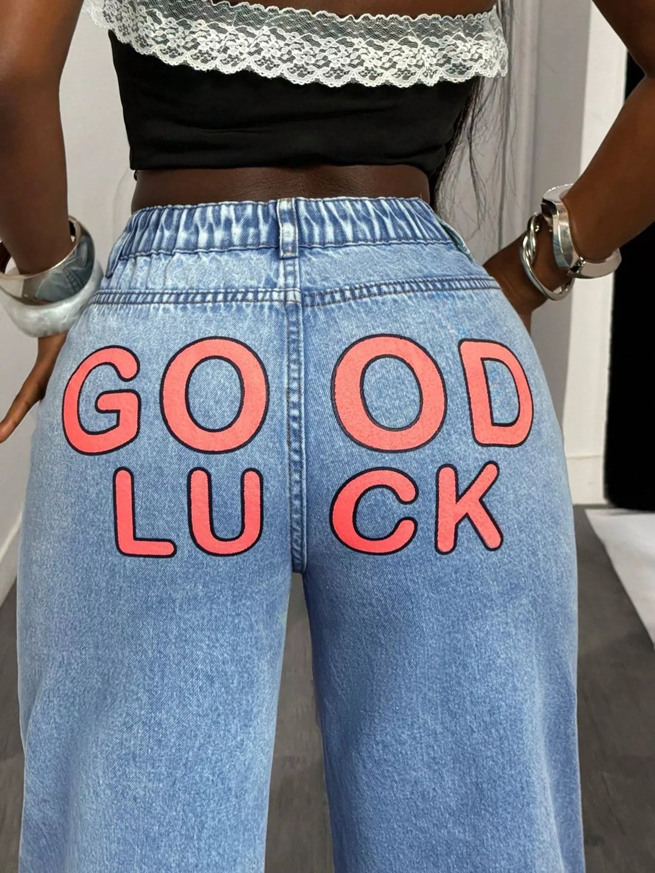 Blue jeans with 'GOOD LUCK' text on the back, worn by a person.
