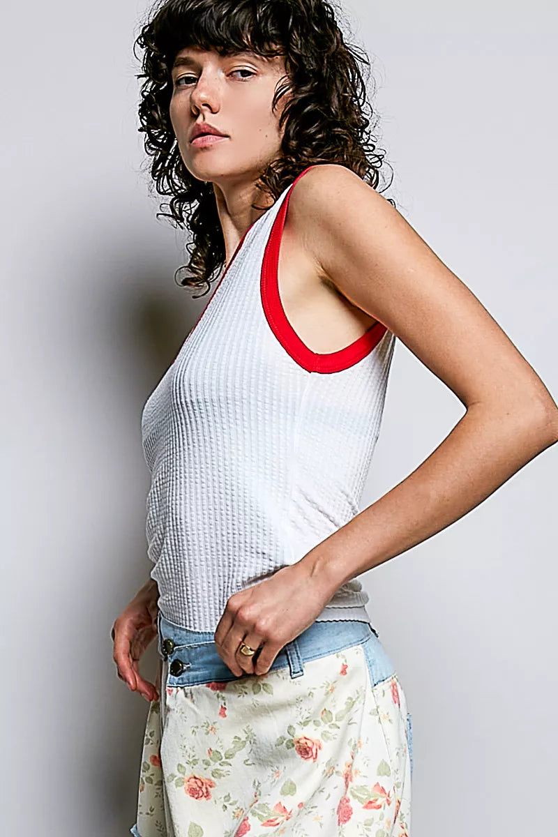 Woman wearing a white tank top with red trim and floral pants against a plain background