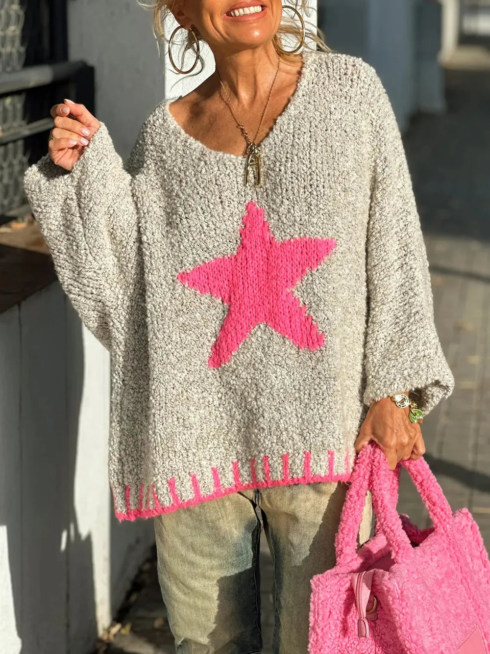 Person wearing a gray sweater with a pink star design, holding a pink bag.